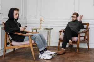 man in black sweater and blue denim jeans sitting on brown wooden rocking chair